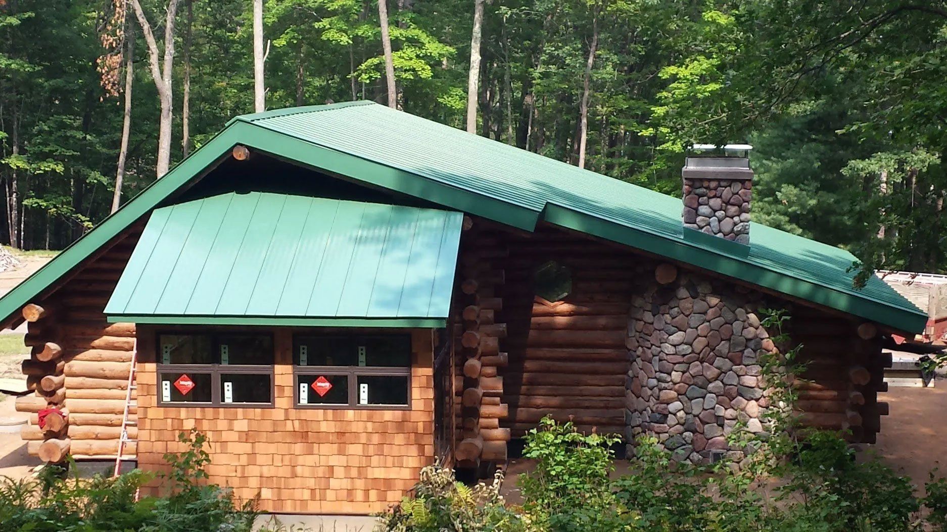 Rustic log cabin with green roof and stone chimney in a forest clearing