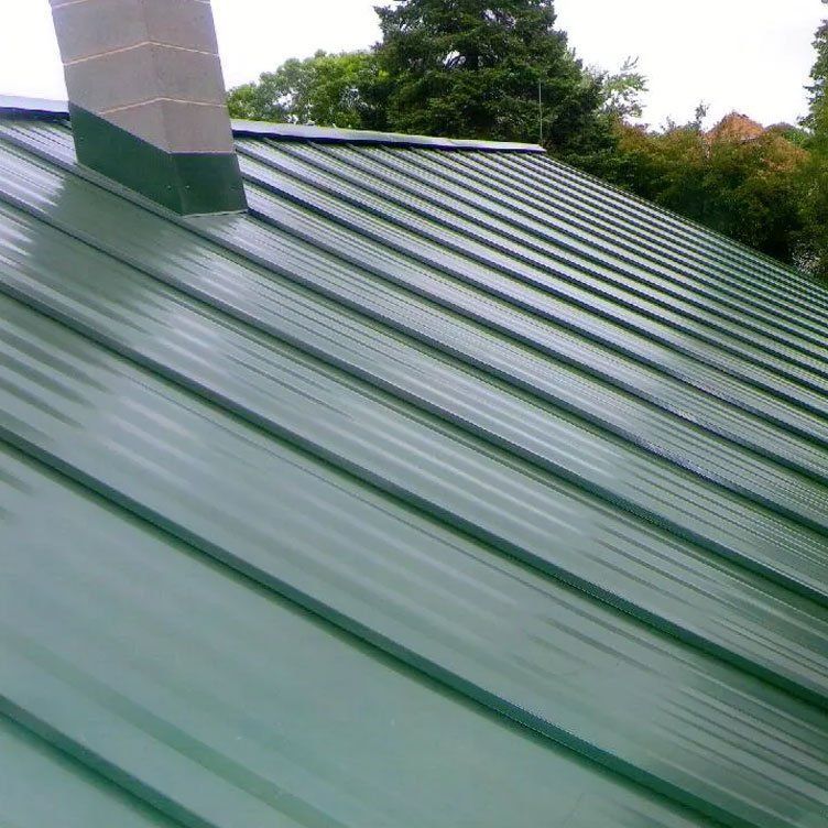 Green metal roof with a chimney, viewed at an angle under trees