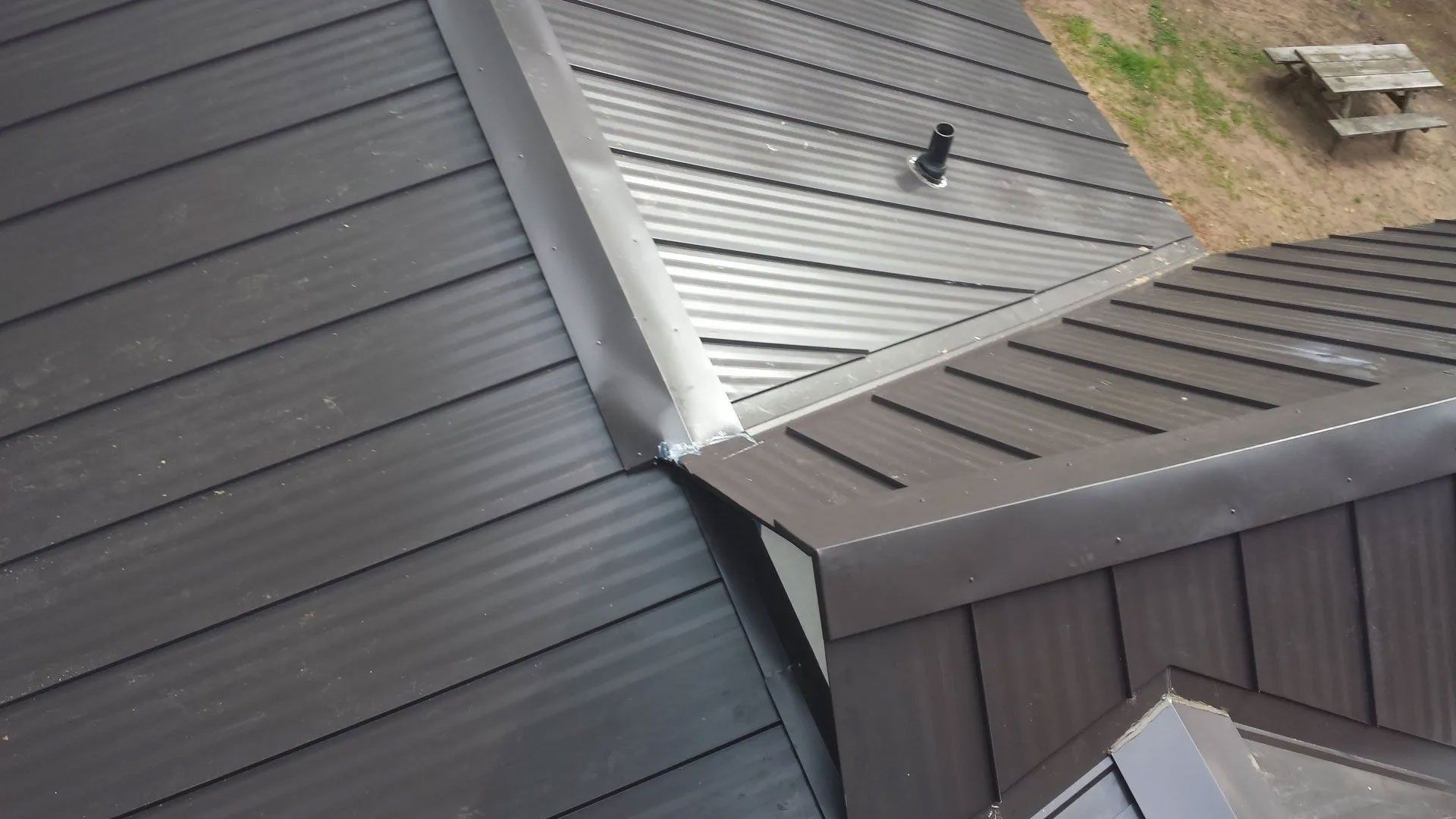 Dark gray metal roof panels meeting at a seam, with a small bird perched on a lighter roof section.