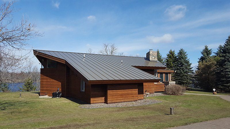 Modern brown wood house with a sloped gray roof in a grassy yard under a blue sky