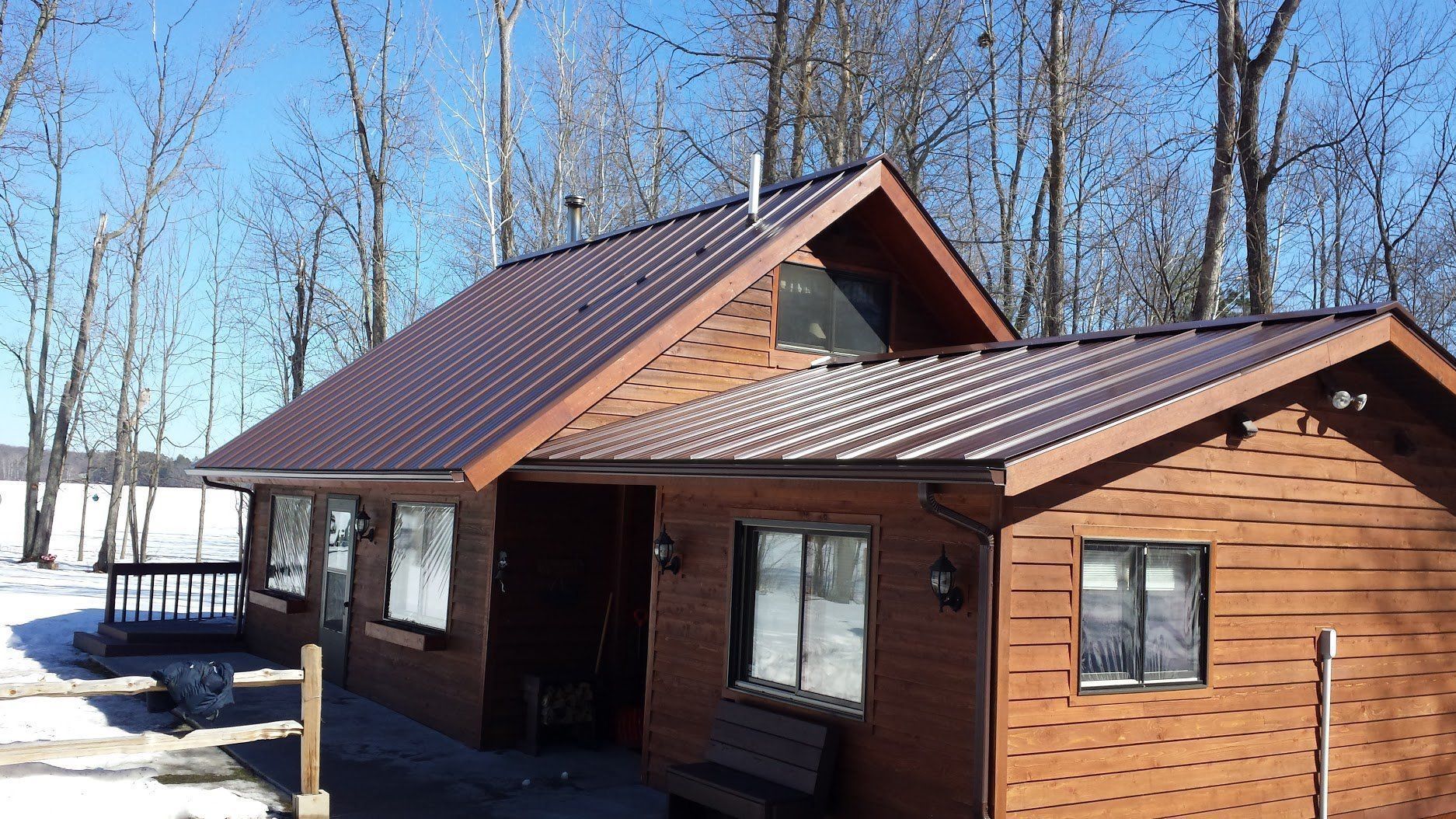 Brown wooden cabin with a dark metal roof in a snowy forest clearing