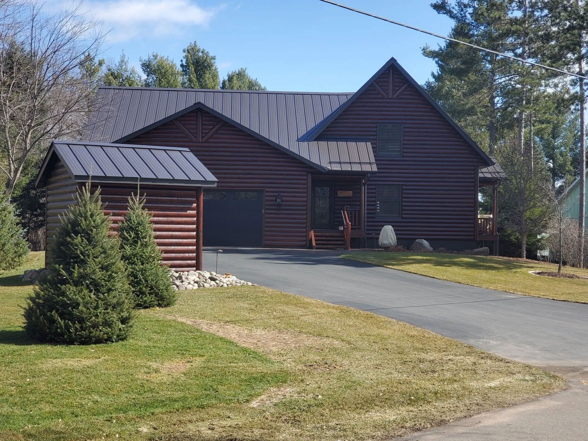 Dark wood house with a metal roof and driveway in a wooded yard