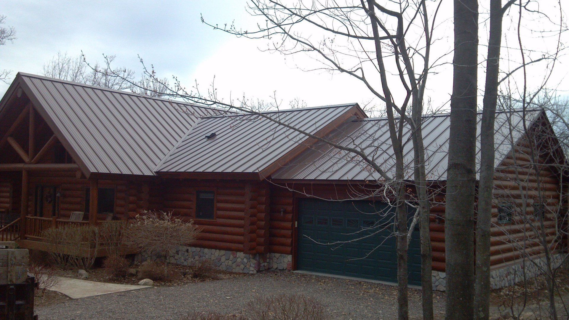 Log cabin-style house with a green garage door and bare trees in front