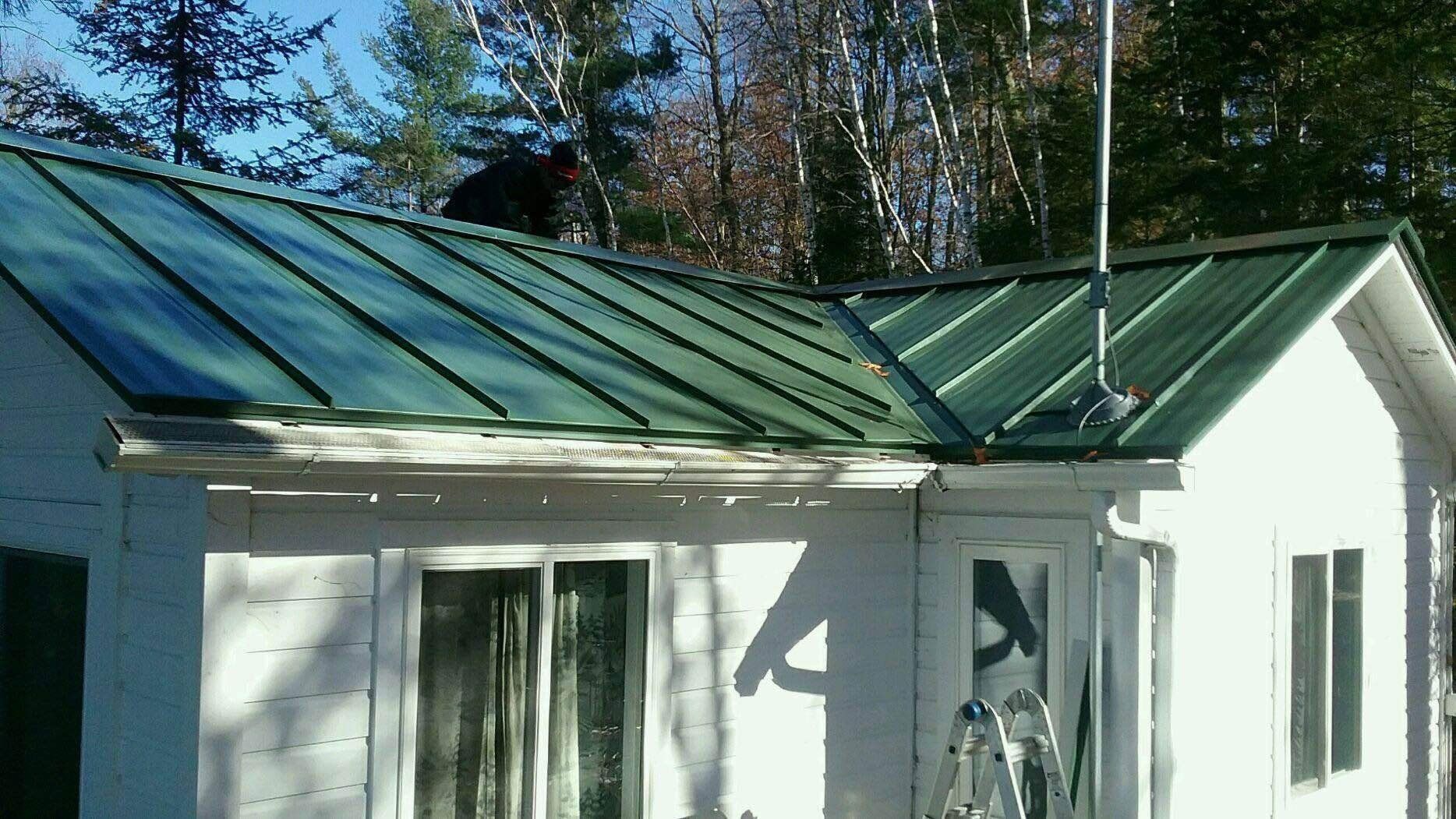Small white house with a green metal roof and a glass-roofed porch in sunlight