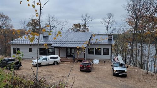 Single-story house with a gray roof and three parked vehicles in a leaf-strewn yard under overcast skies