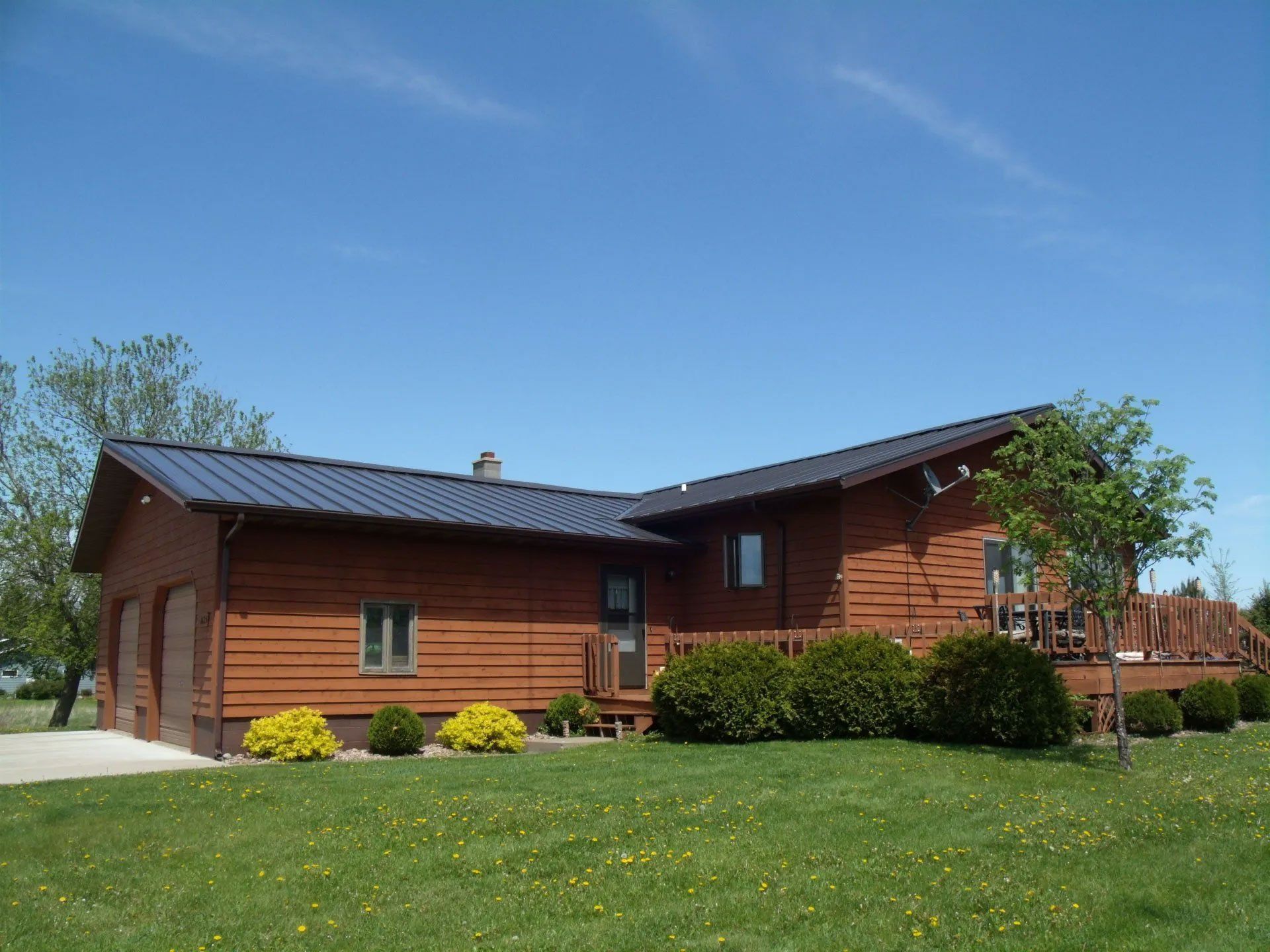 Single-story brown house with a dark roof and green lawn under a blue sky
