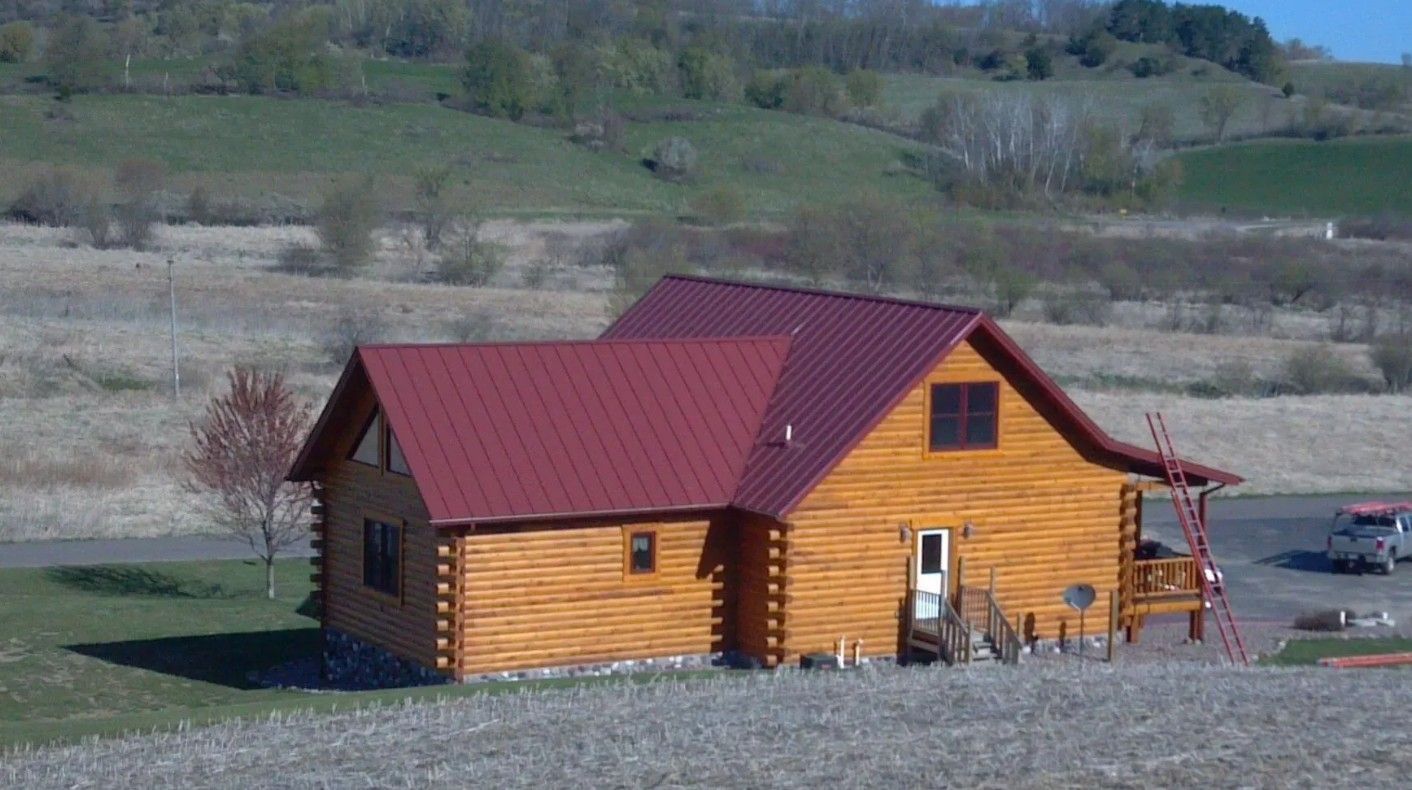Log cabin with red roof in a rural field with mountains in the background