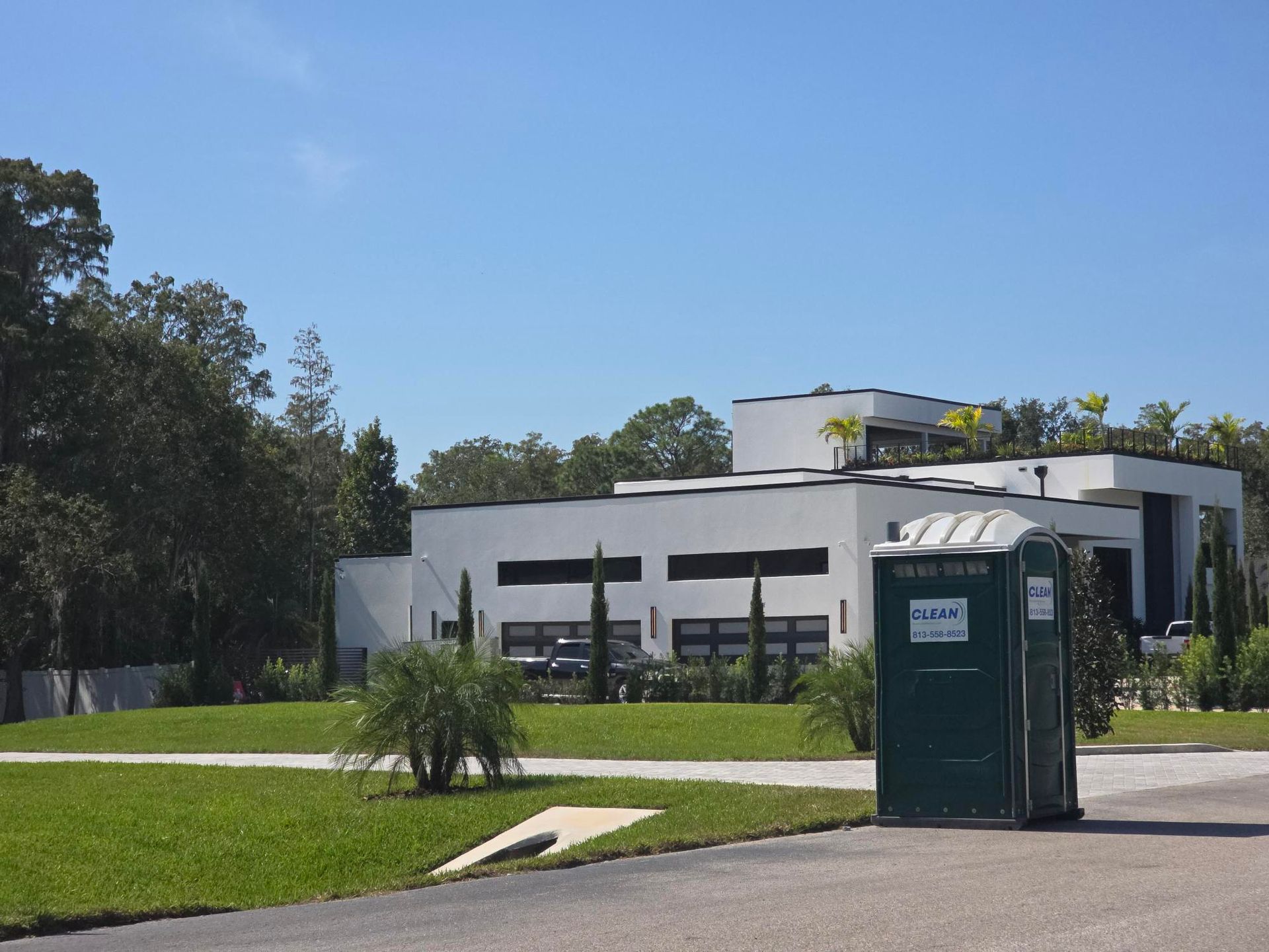 Green portable toilets in front of a modern white building on a sunny day.