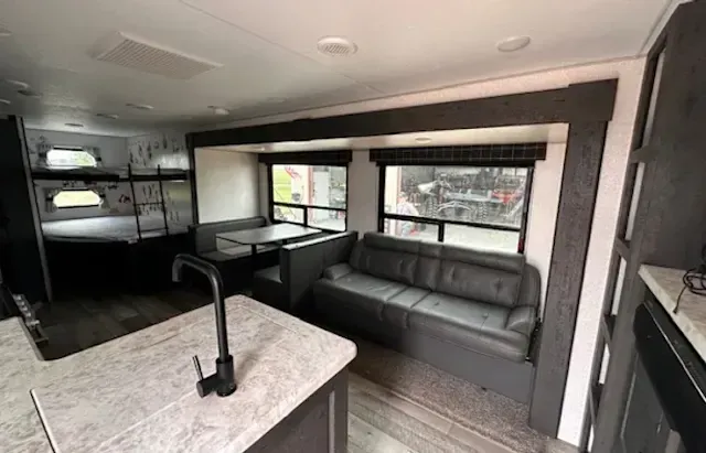 A rv with a couch , table , sink and bunk beds.