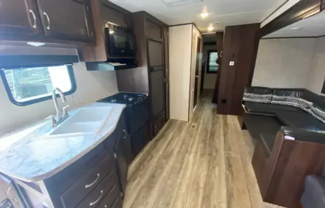 A kitchen in a rv with a sink , stove and microwave.