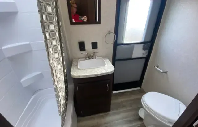 A bathroom with a sink , toilet , shower and mirror.