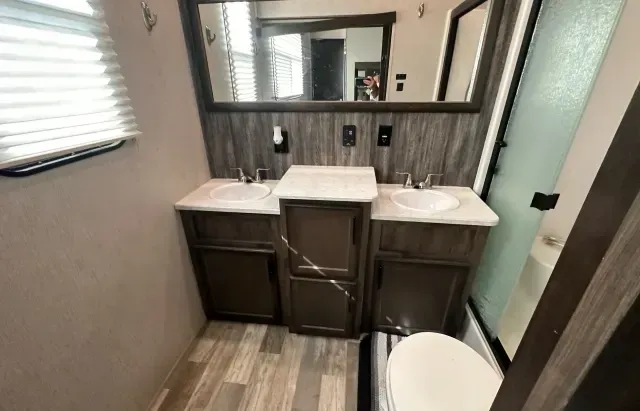 A bathroom with two sinks , a toilet and a mirror.