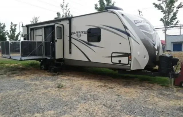 A rv is parked in a gravel lot with trees in the background
