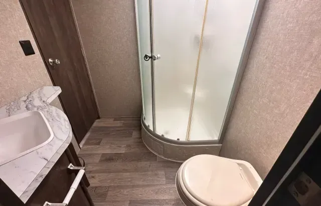 A bathroom with a toilet , sink and shower.