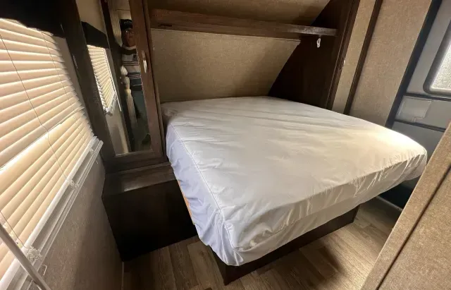 A bed in a rv with a white mattress and a mirror.