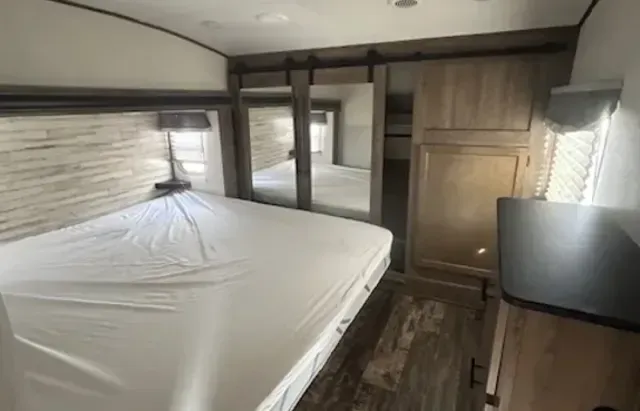 A bedroom in a trailer with a bed and a dresser.