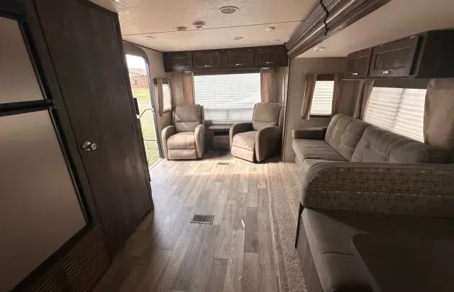 A living room in a rv with a couch , chairs and a refrigerator.