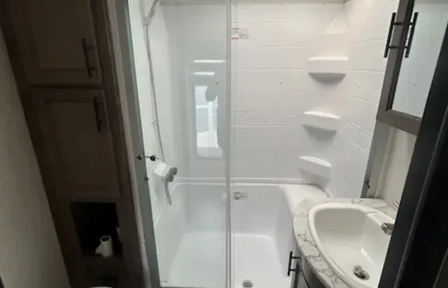 A bathroom with a sink , shower , and window.