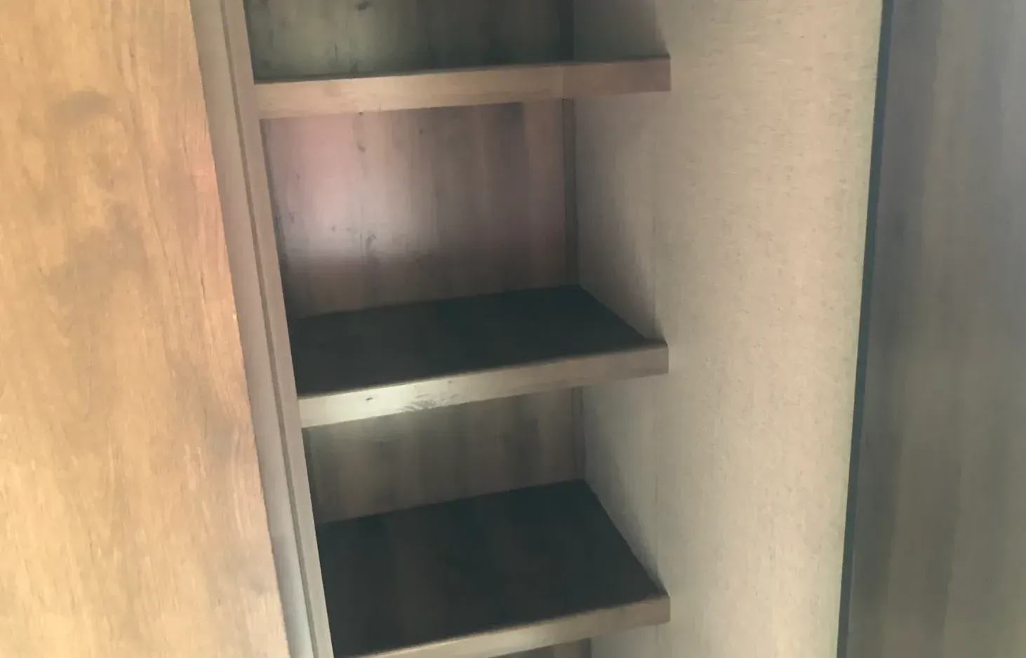 A wooden shelf with three shelves in a closet.