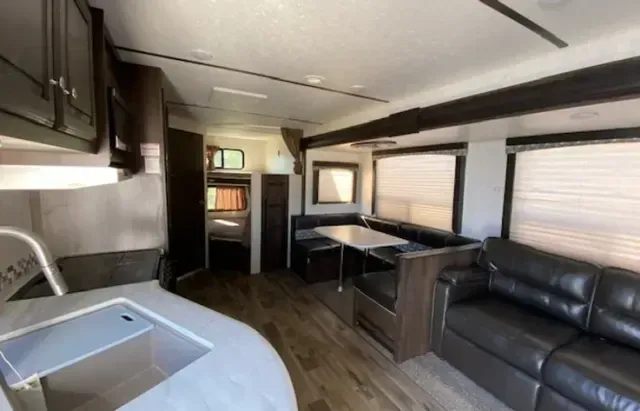 A living room in a rv with a couch , table and sink.
