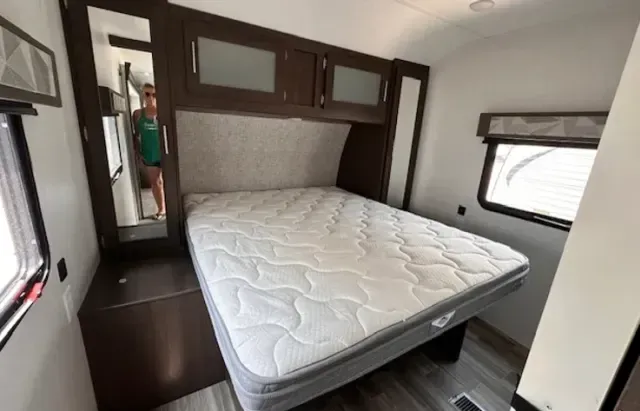 A bedroom in a trailer with a bed and a mirror.