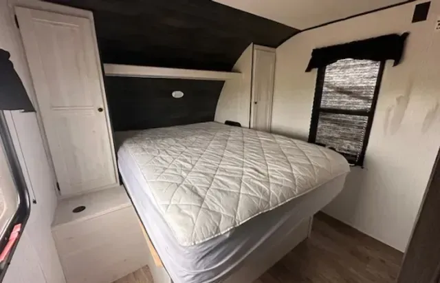 A bedroom in a trailer with a bed and a window.