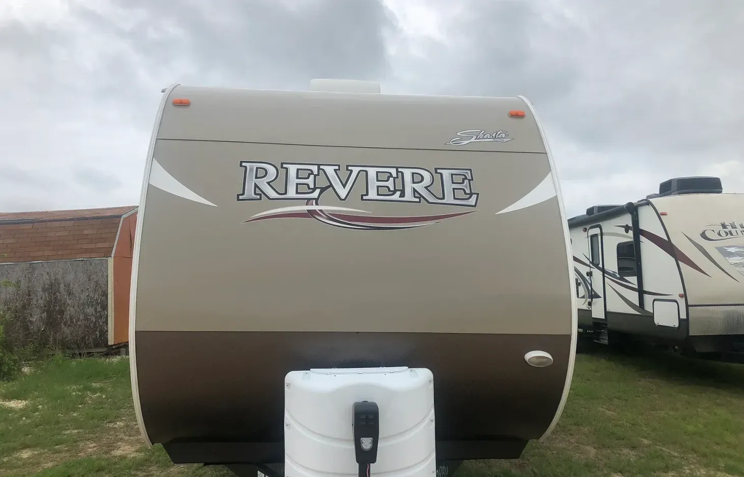 A rv is parked in a grassy field in front of a building.