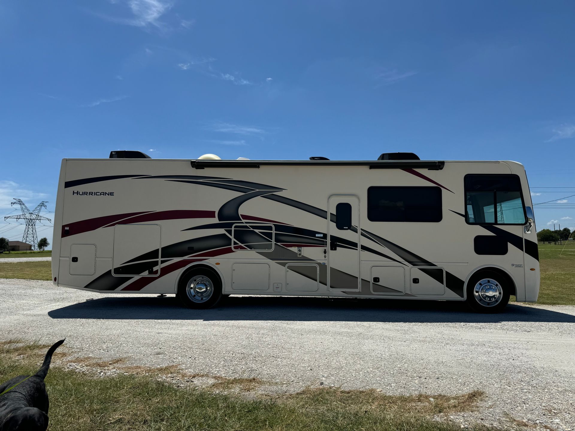 A large white and red rv is parked on the side of a gravel road.