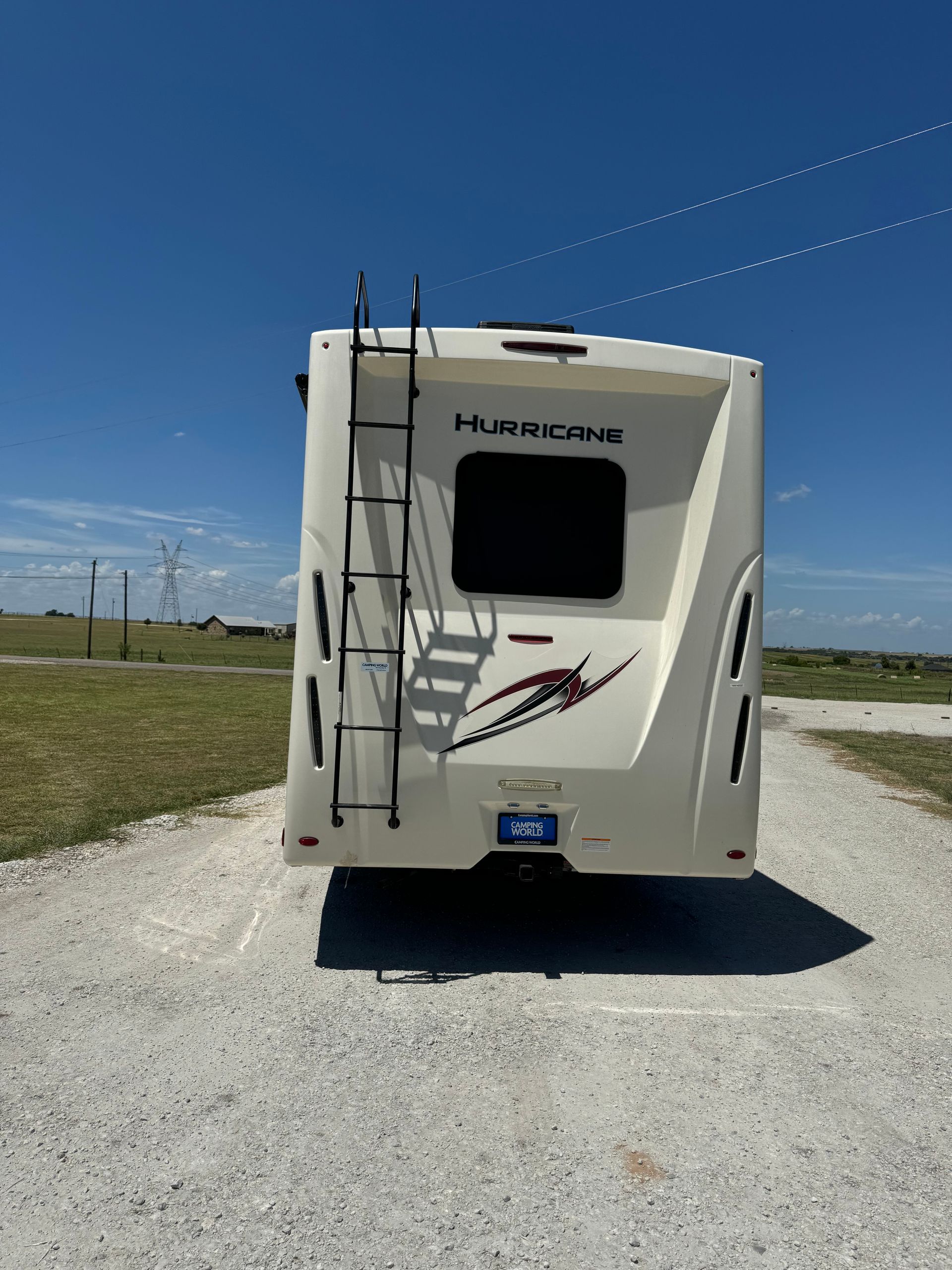 A white rv with a ladder on the back is parked on a gravel road.