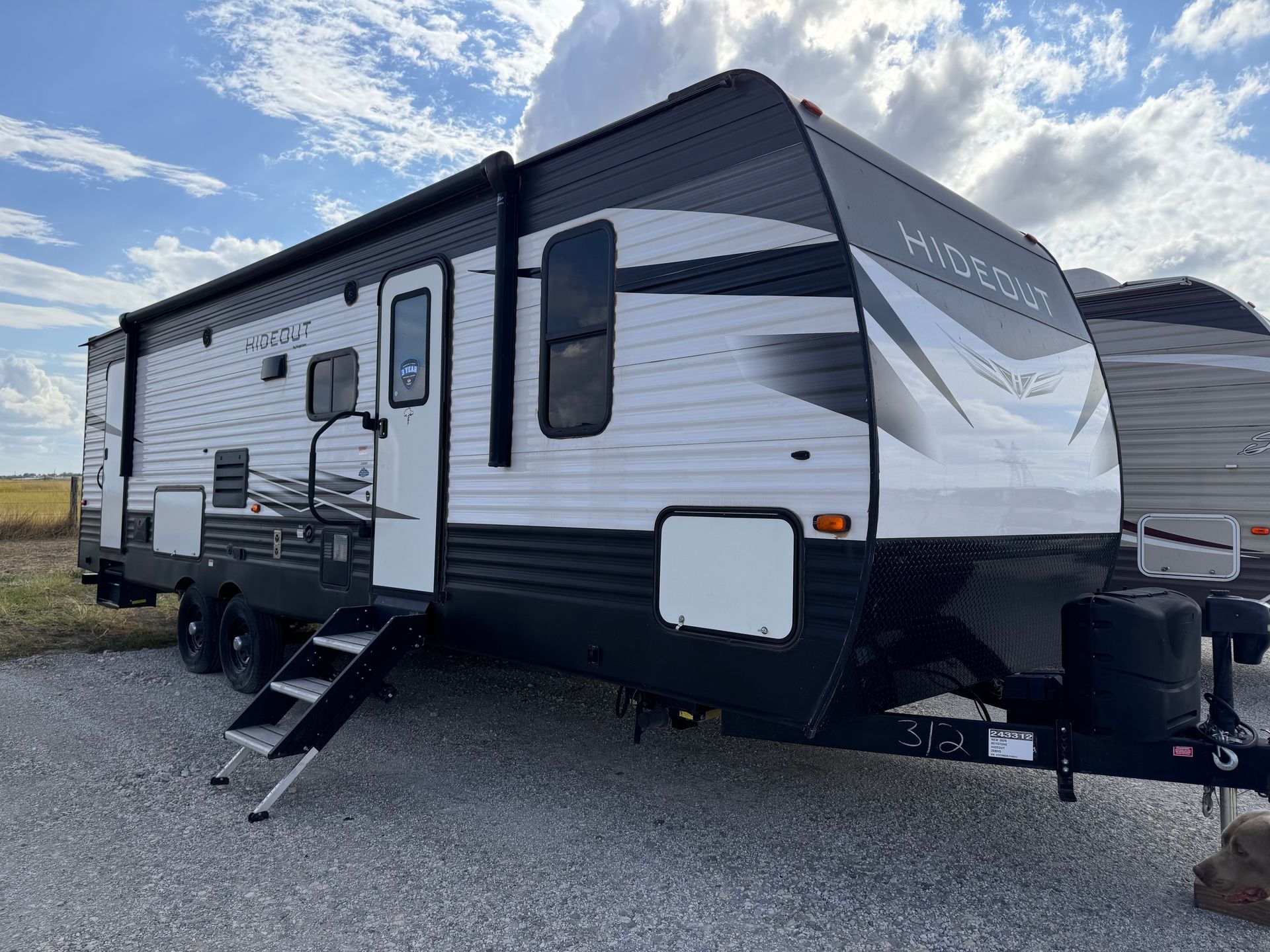 A white and black trailer is parked in a gravel lot.