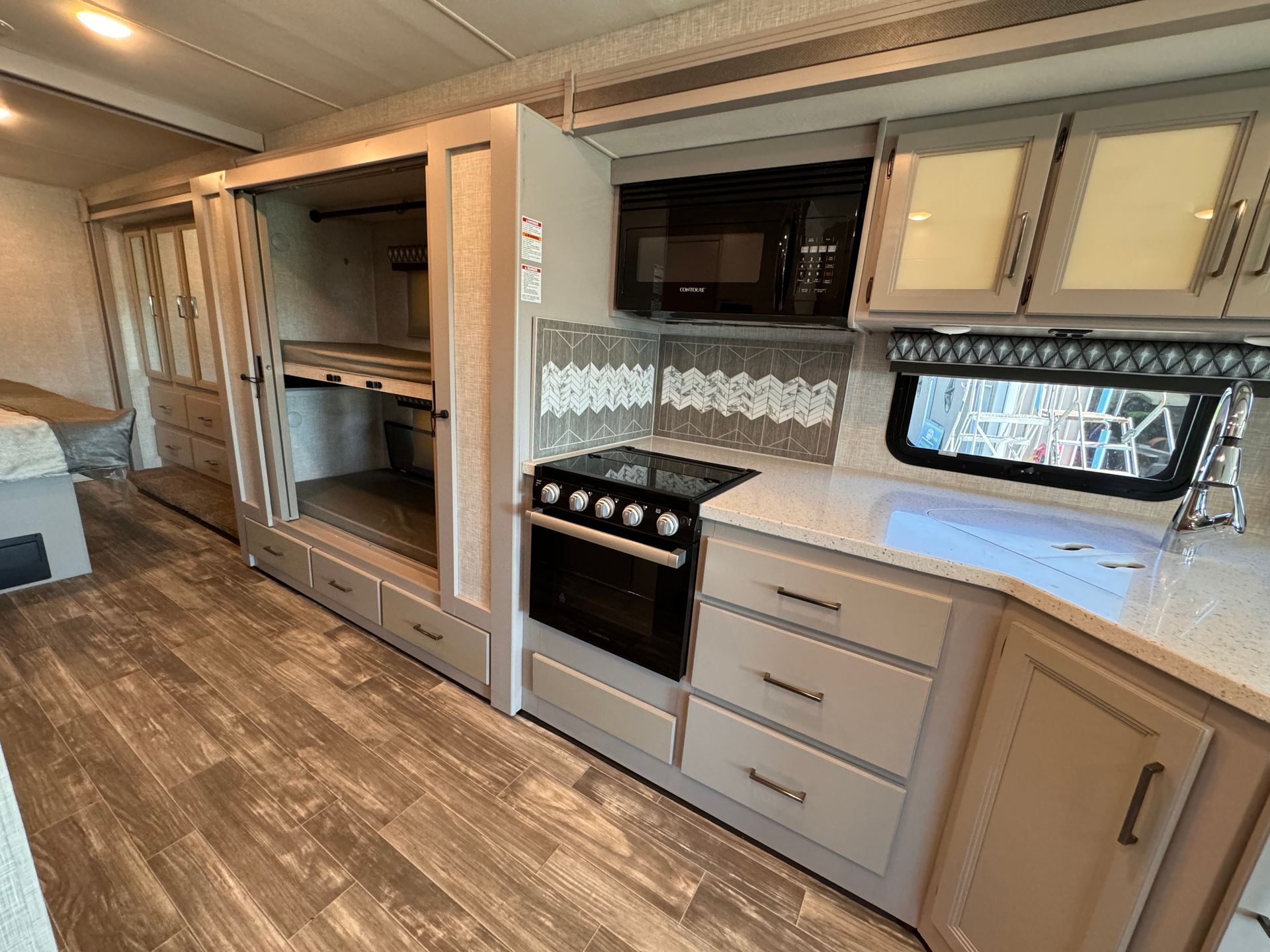 A kitchen in a rv with a stove , microwave , sink and cabinets.