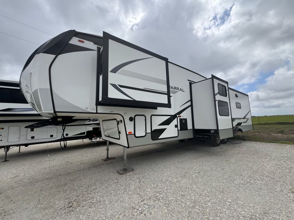 A white and black trailer is parked in a gravel lot.