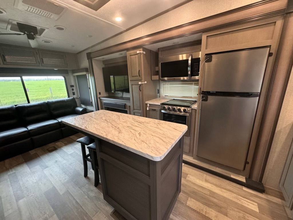 A kitchen in a rv with a stainless steel refrigerator , stove , microwave and a large island.