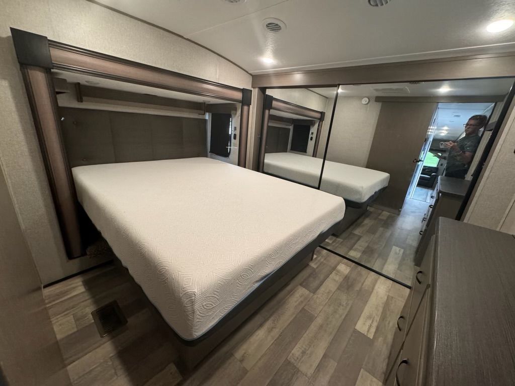 A bedroom with a bed , mirrors and a dresser.