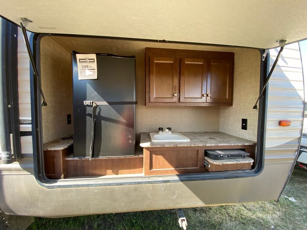 A trailer with a refrigerator , sink , and cabinets.