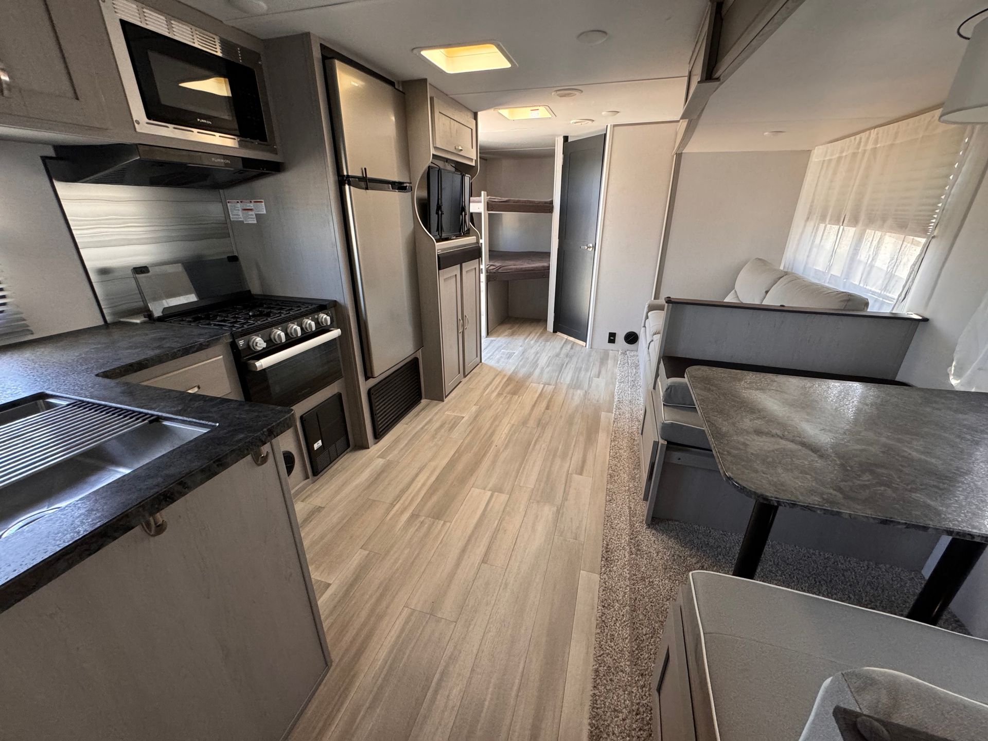 A kitchen in a rv with a stove , sink , and microwave.