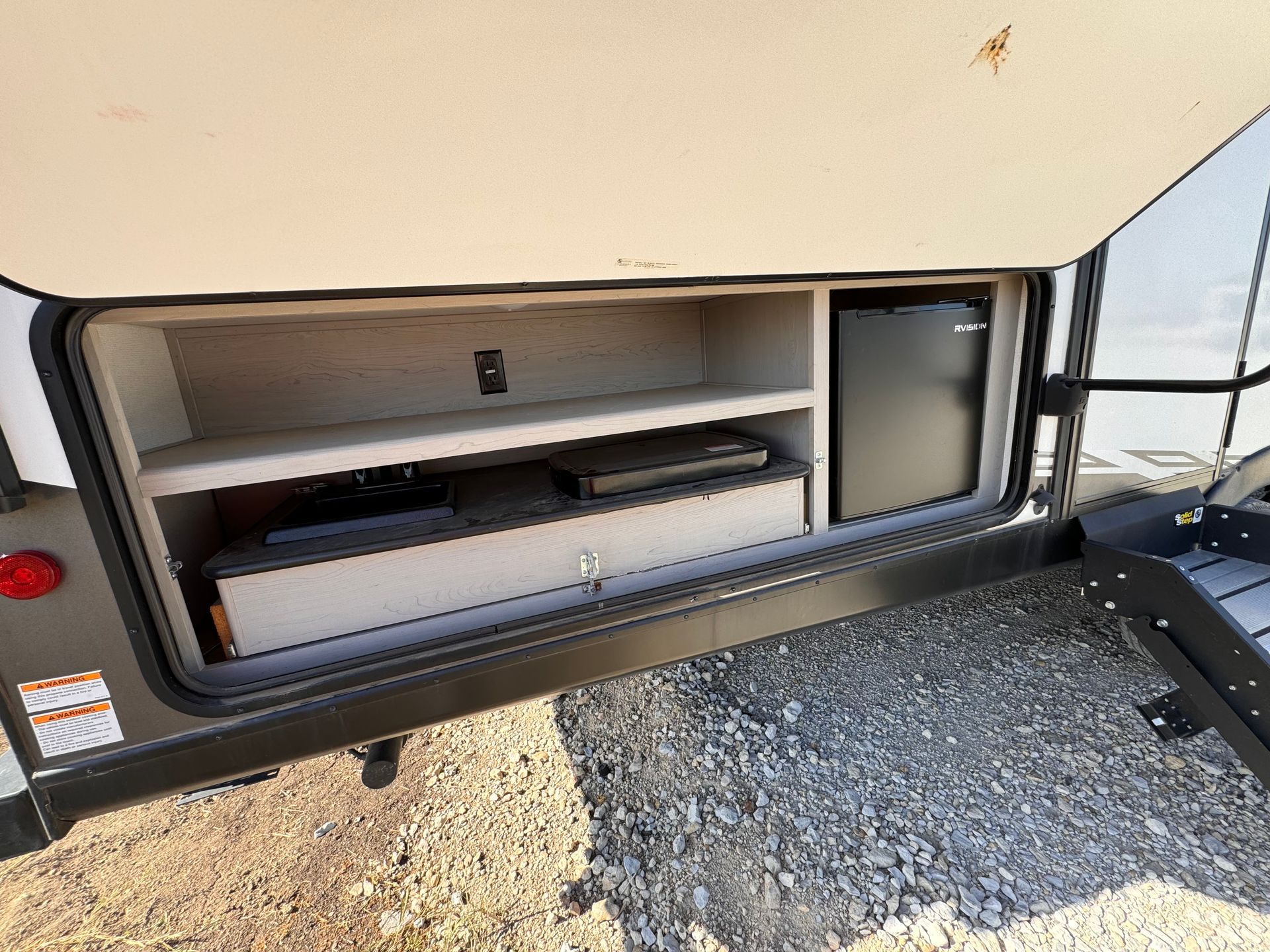 The back of a trailer with a refrigerator and shelves in it.