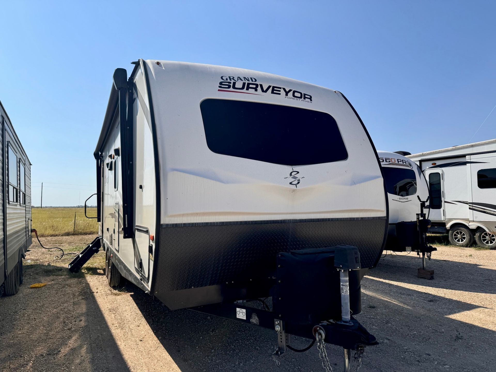 A white surveyor trailer is parked in a gravel lot.