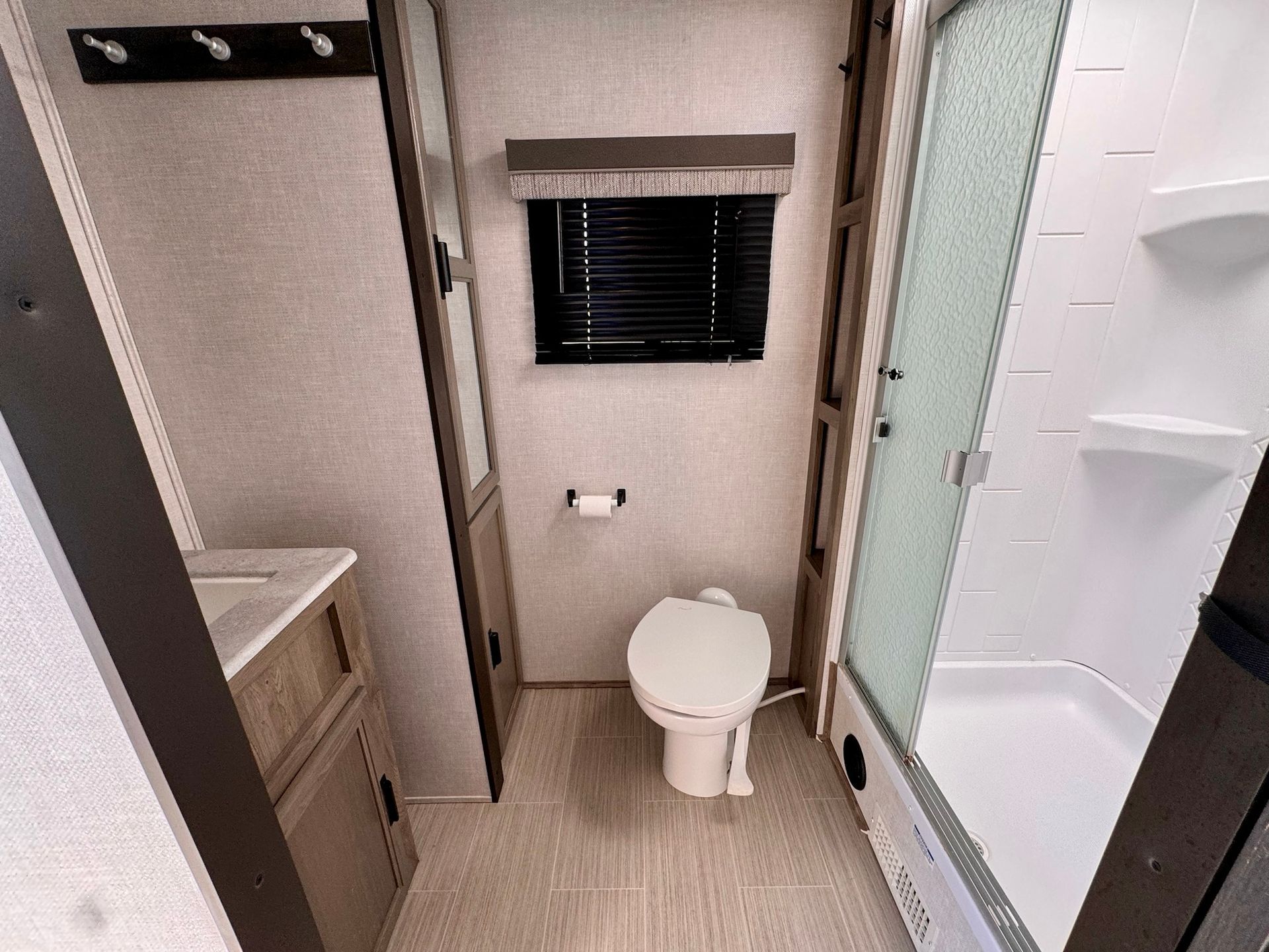 A bathroom with a toilet , sink , shower and window.