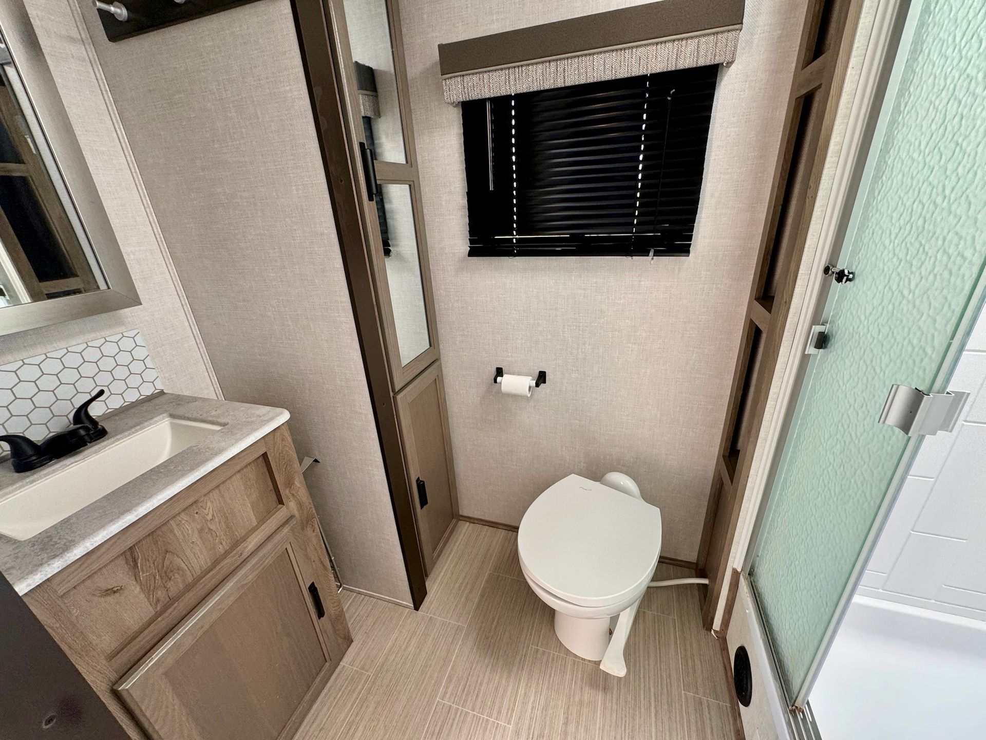 A bathroom with a toilet , sink , mirror and window.