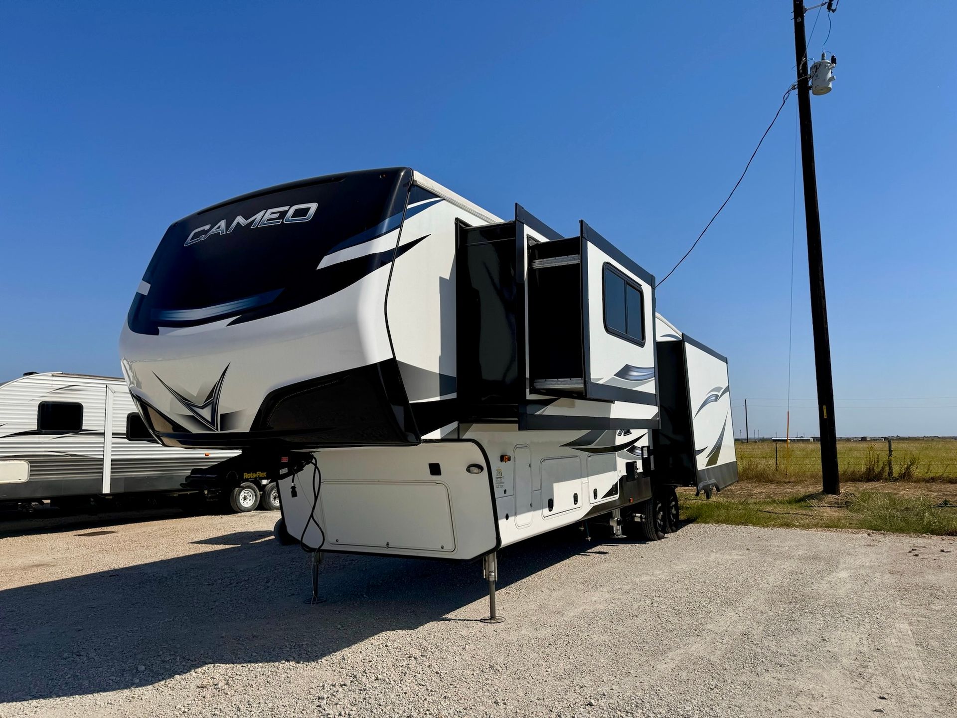 A white rv is parked in a gravel lot next to a power pole.