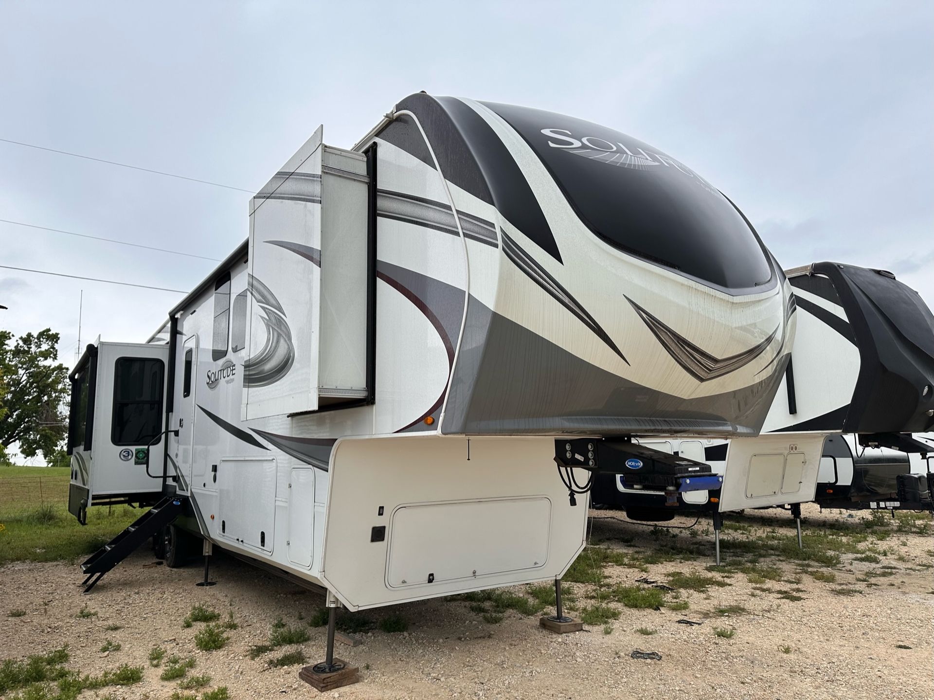 A white and black rv is parked in a gravel lot.