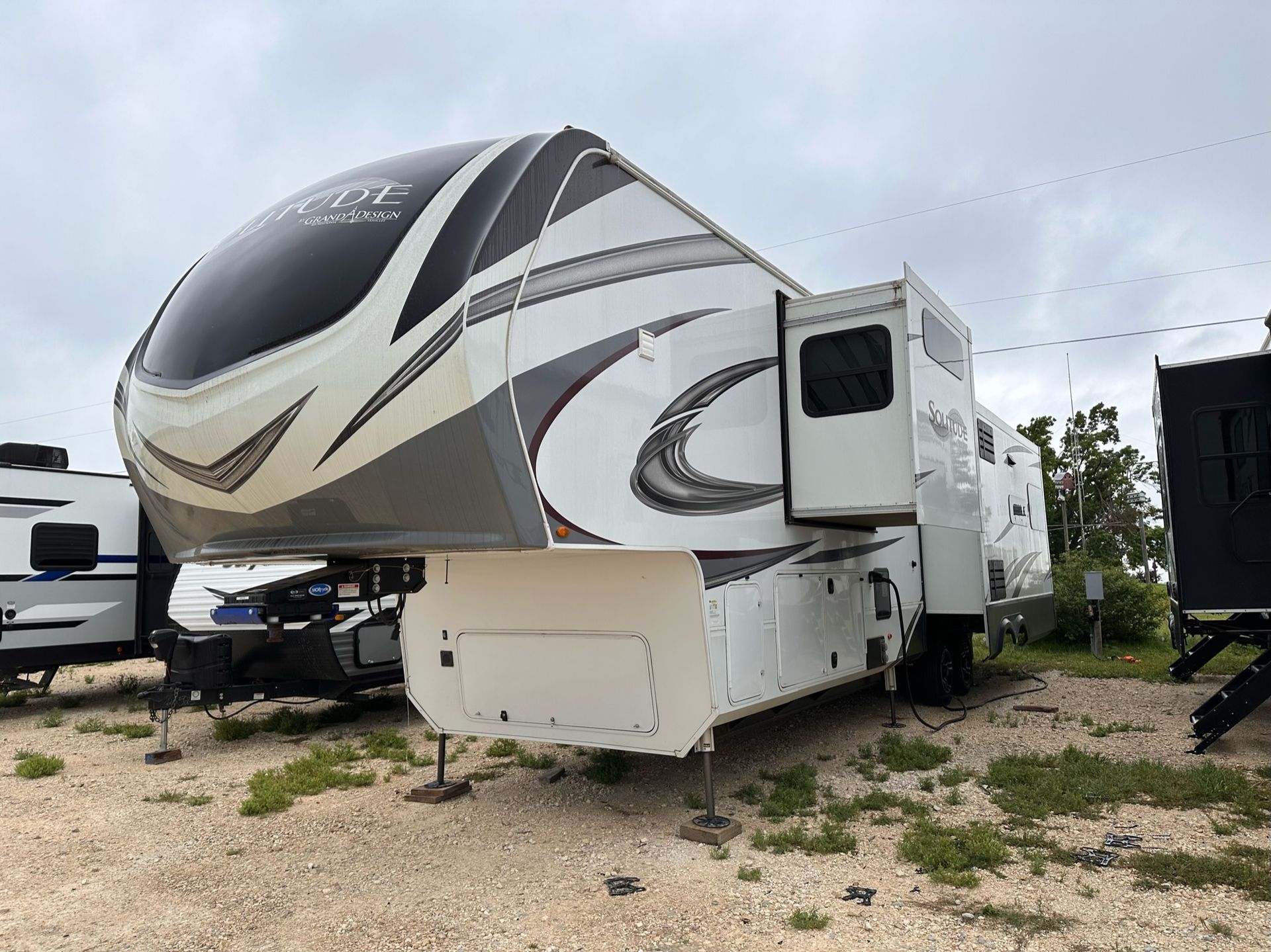 A white and gray rv is parked in a gravel lot.