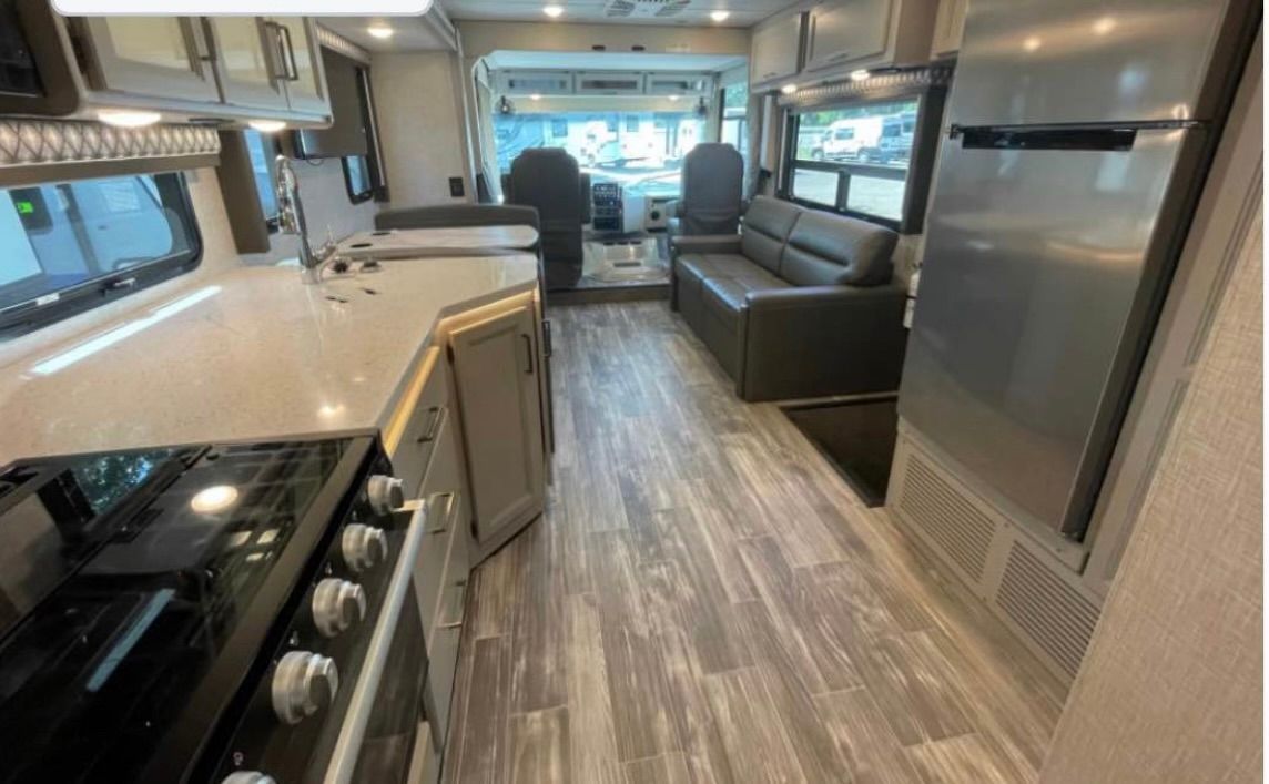 The inside of a rv with a stove , refrigerator , couch , and living room.