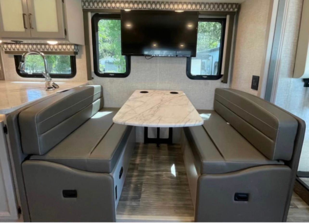 A rv with a table and benches and a flat screen tv