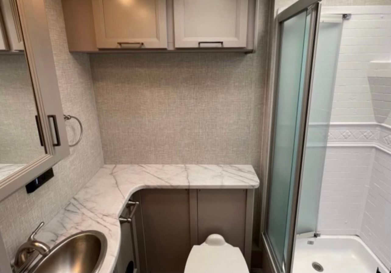 A bathroom with a toilet , sink and shower.