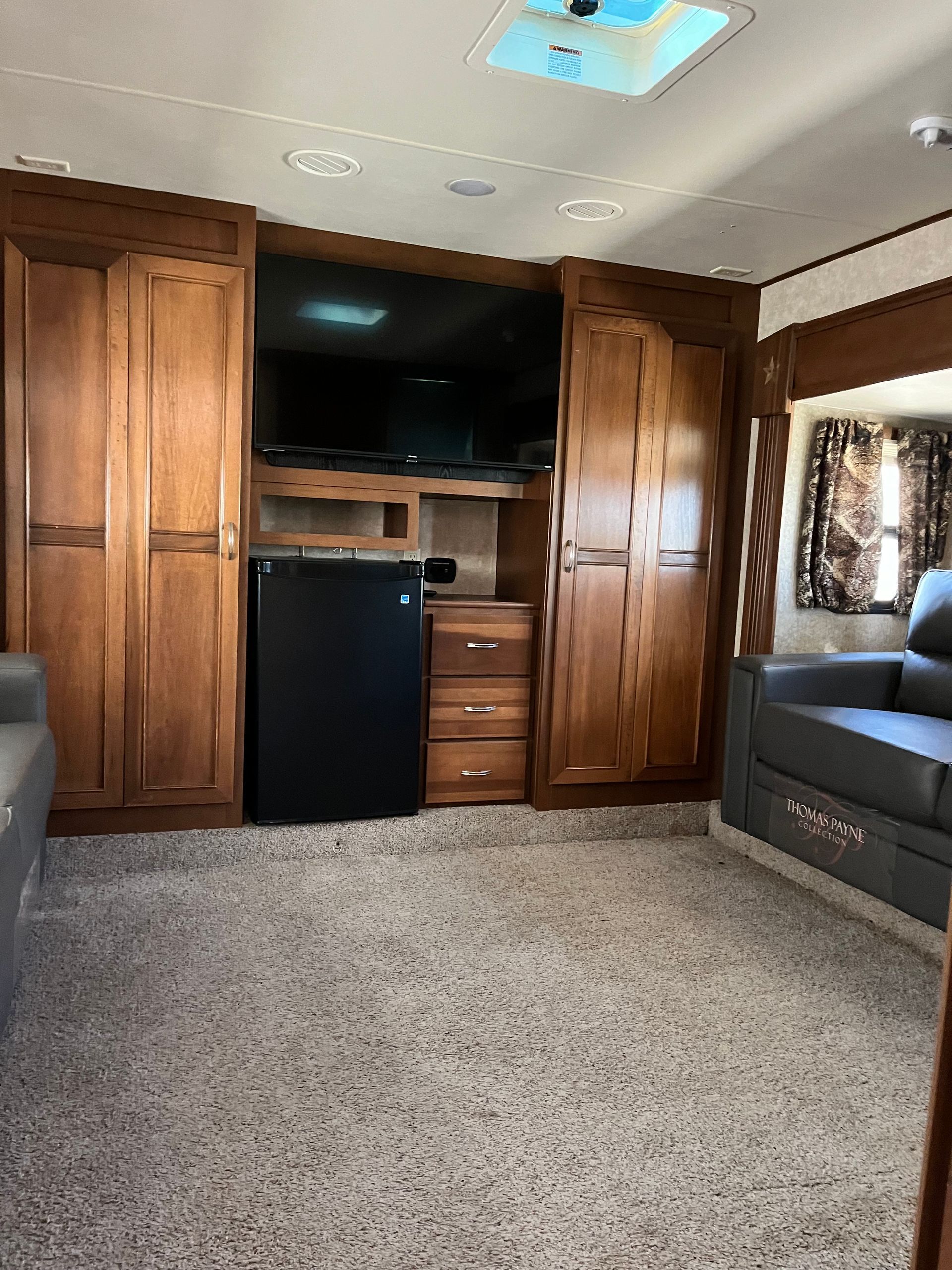A living room in a trailer with a couch , television , refrigerator and cabinets.