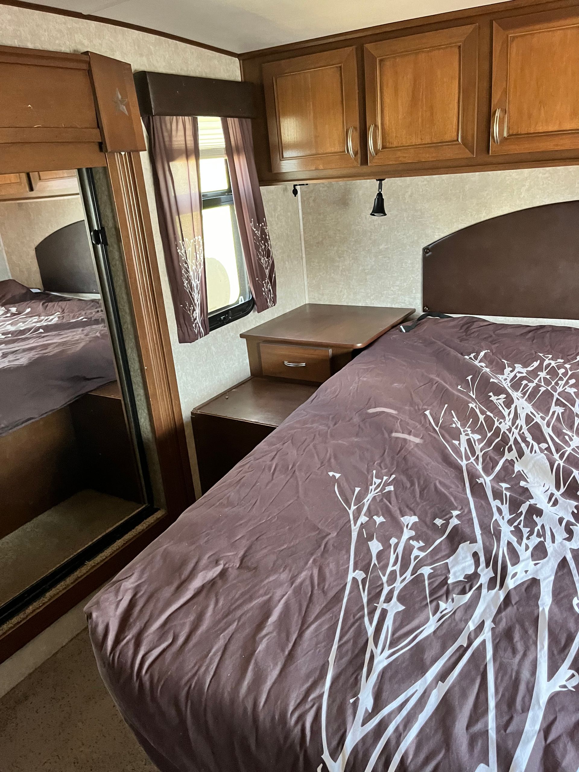 A bedroom in a rv with a bed and a mirror.