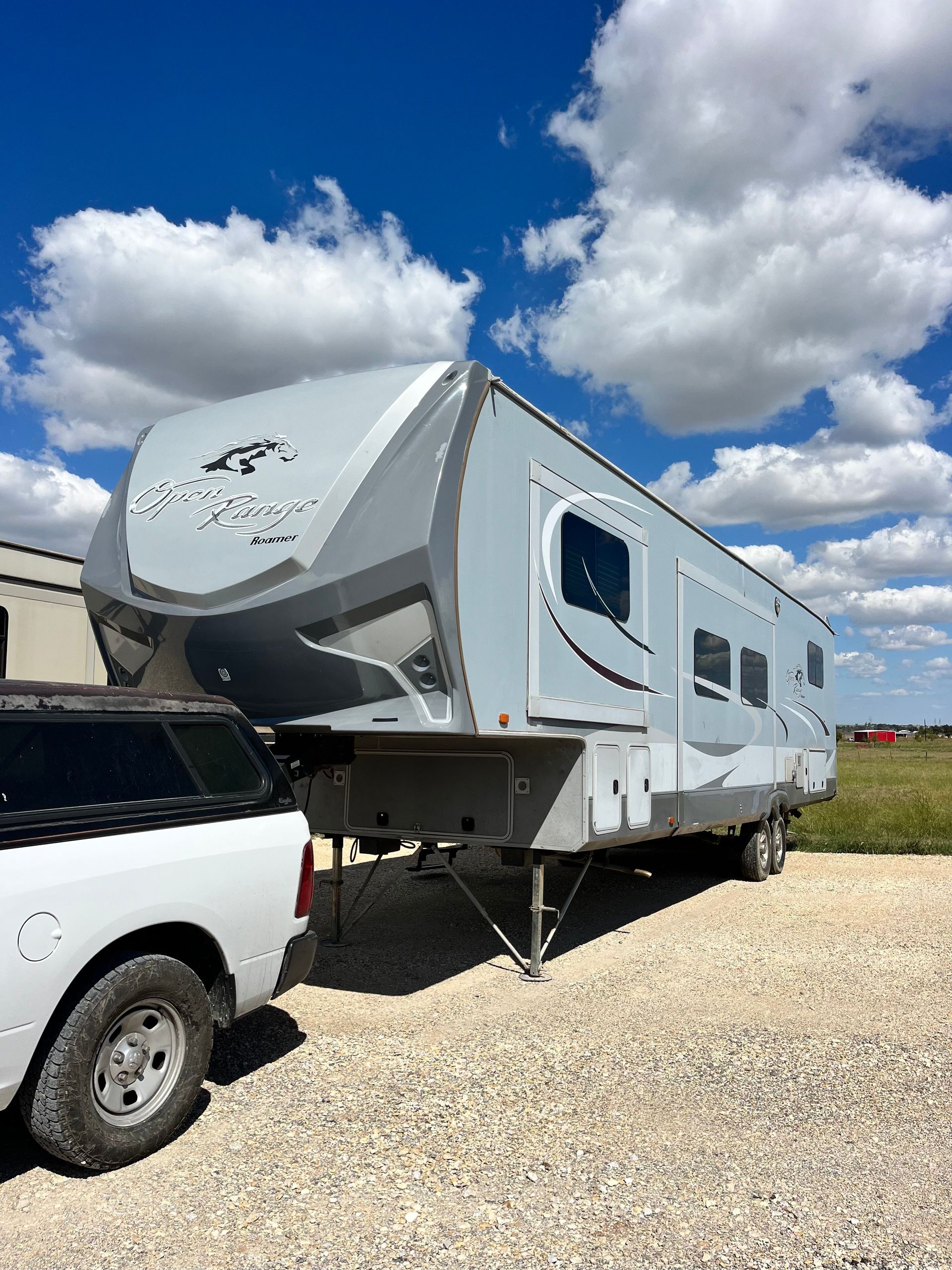 A white truck is towing a trailer in a gravel lot.