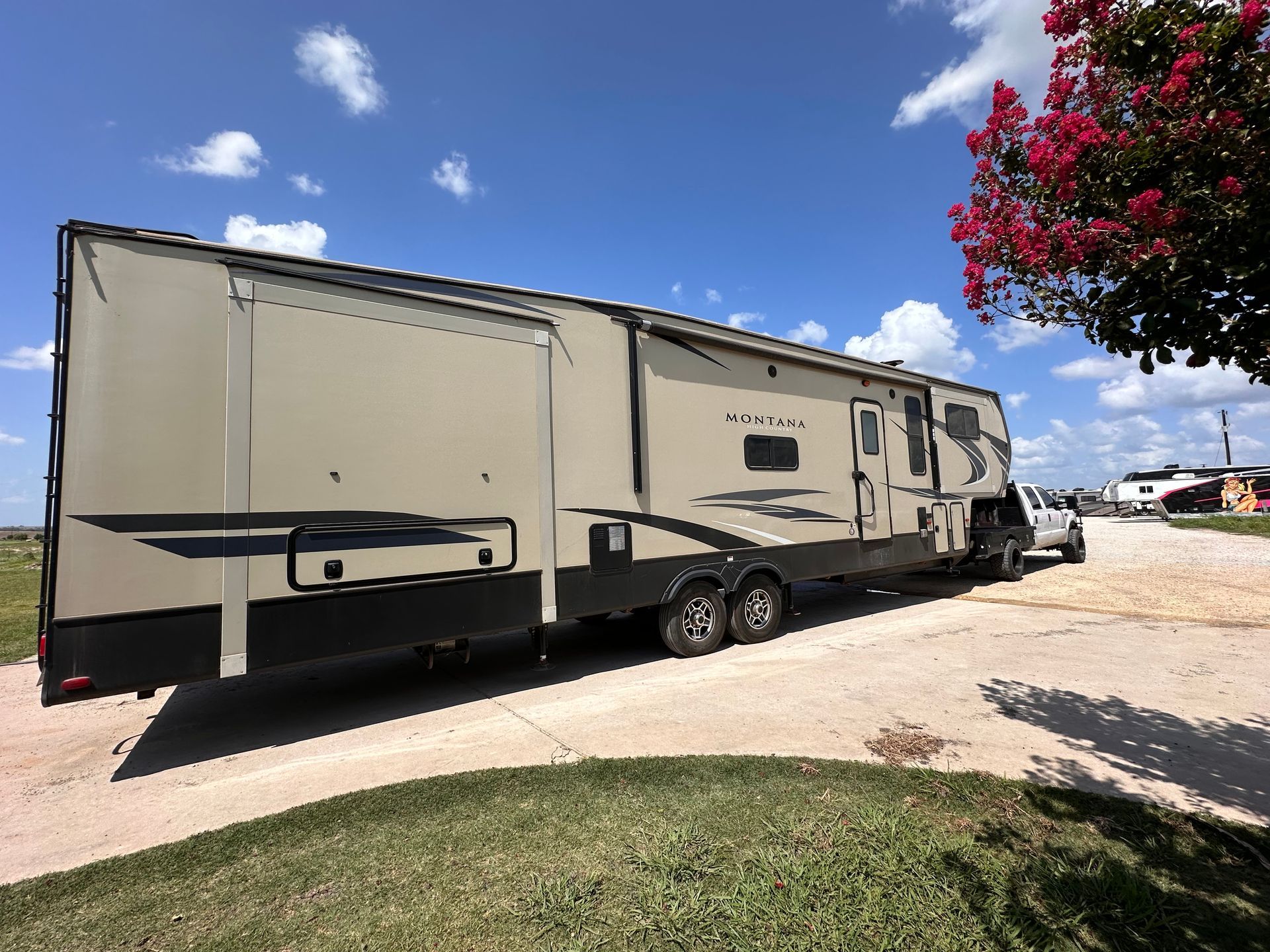 A large rv is parked on the side of the road next to a tree.